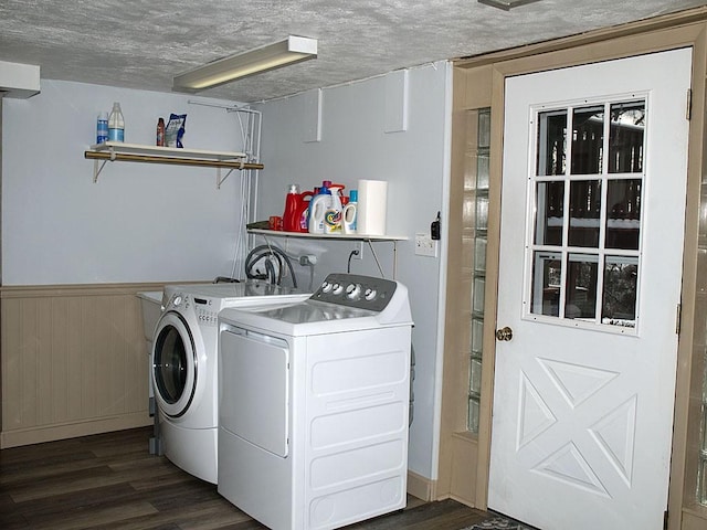 clothes washing area featuring a textured ceiling, dark hardwood / wood-style flooring, washer and clothes dryer, and wooden walls