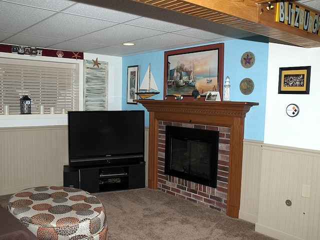 carpeted living room featuring wood walls, a brick fireplace, and a drop ceiling