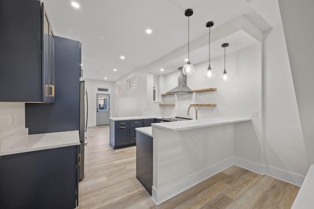 kitchen with light wood-type flooring, kitchen peninsula, wall chimney range hood, and pendant lighting