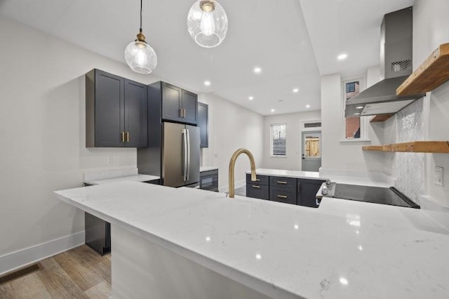 kitchen featuring light hardwood / wood-style floors, stainless steel fridge, kitchen peninsula, wall chimney range hood, and pendant lighting