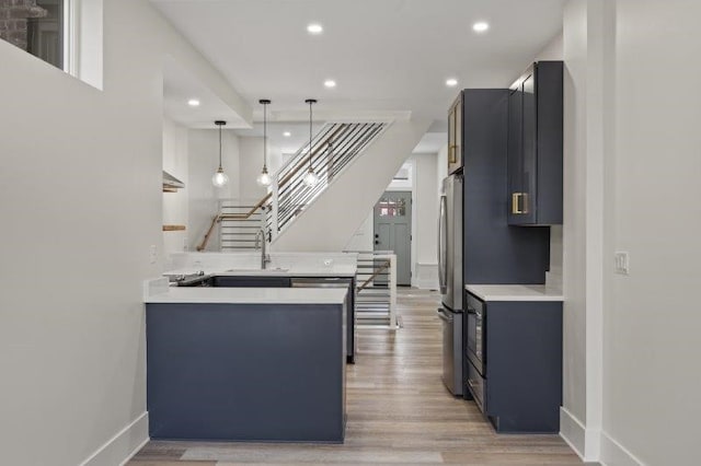 kitchen featuring light hardwood / wood-style floors, pendant lighting, kitchen peninsula, sink, and appliances with stainless steel finishes