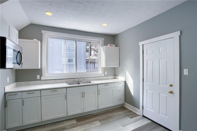 kitchen with vaulted ceiling, light hardwood / wood-style floors, sink, a textured ceiling, and white cabinets