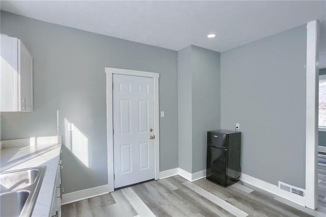 interior space featuring black refrigerator, light wood-type flooring, sink, and white cabinetry