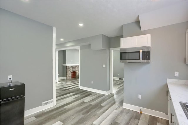 kitchen with white cabinetry, black refrigerator, a stone fireplace, light wood-type flooring, and light stone countertops