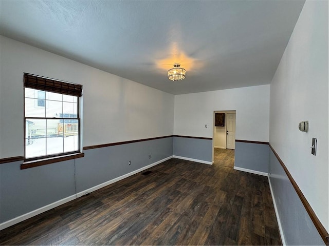 spare room with dark hardwood / wood-style floors and a notable chandelier