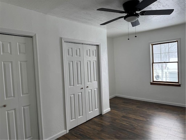 unfurnished bedroom featuring a textured ceiling, ceiling fan, dark hardwood / wood-style floors, and multiple closets