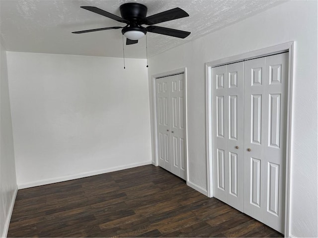 unfurnished bedroom featuring ceiling fan, multiple closets, dark hardwood / wood-style flooring, and a textured ceiling