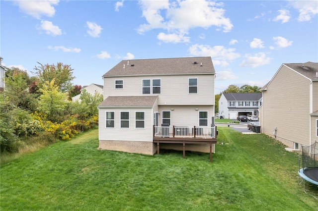 rear view of property featuring a wooden deck, a yard, and a trampoline