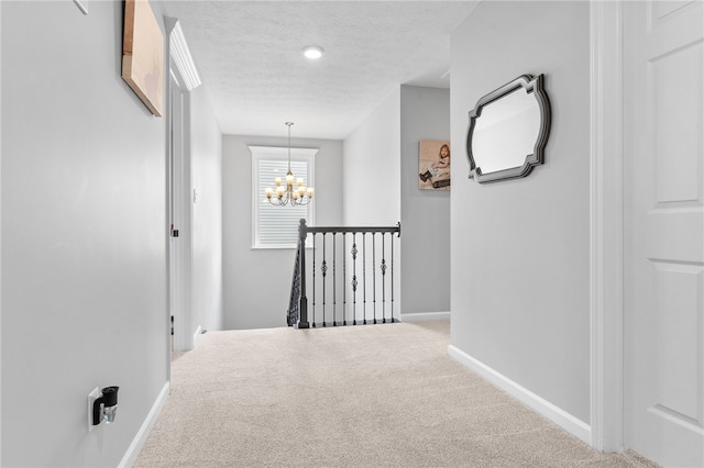 corridor featuring carpet, a textured ceiling, and a chandelier