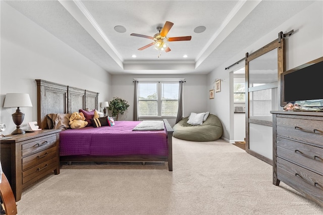 carpeted bedroom with ceiling fan, ornamental molding, a raised ceiling, and a barn door