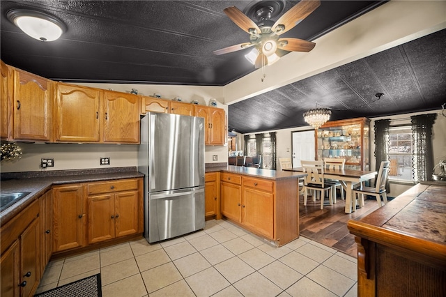 kitchen featuring light tile patterned floors, kitchen peninsula, stainless steel fridge, and ceiling fan with notable chandelier