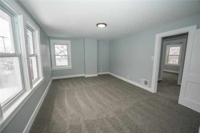 unfurnished room featuring plenty of natural light and dark carpet