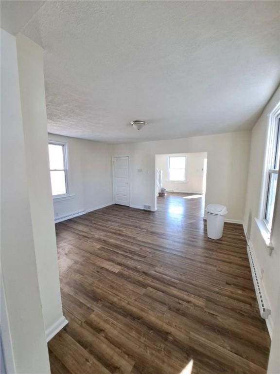 unfurnished living room featuring baseboard heating, dark hardwood / wood-style flooring, plenty of natural light, and a textured ceiling