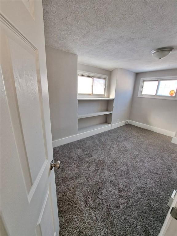 carpeted spare room featuring a textured ceiling, a wealth of natural light, and built in shelves