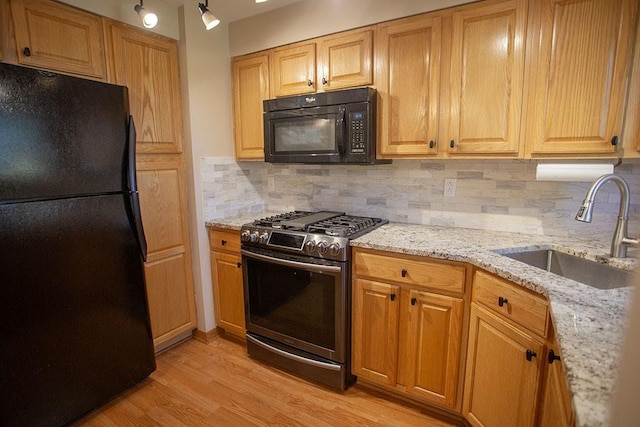 kitchen featuring tasteful backsplash, light stone countertops, black appliances, light hardwood / wood-style flooring, and sink