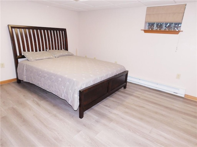 bedroom featuring light wood-type flooring, baseboard heating, and a drop ceiling