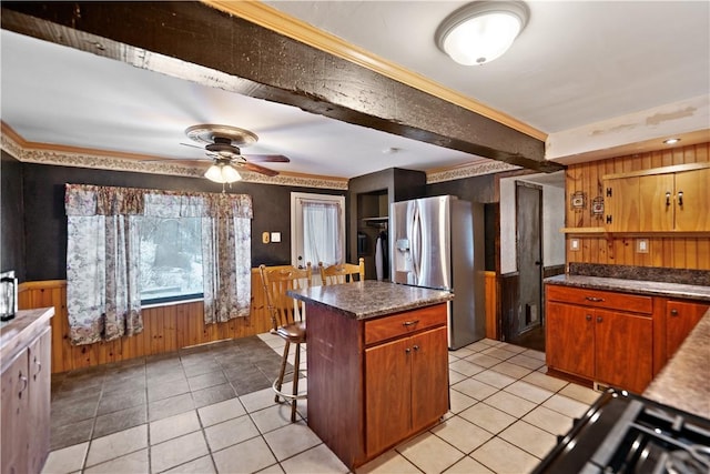 kitchen with dark countertops, stainless steel fridge with ice dispenser, light tile patterned flooring, a kitchen island, and a kitchen bar