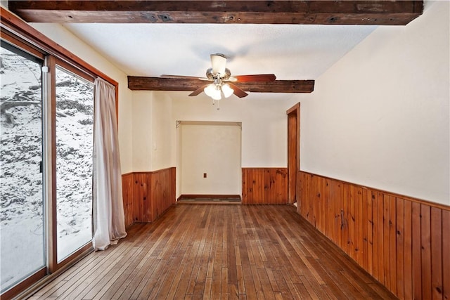 spare room featuring beam ceiling, wainscoting, and wood walls