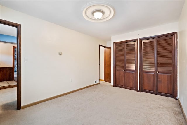 unfurnished bedroom featuring light colored carpet, baseboards, and two closets