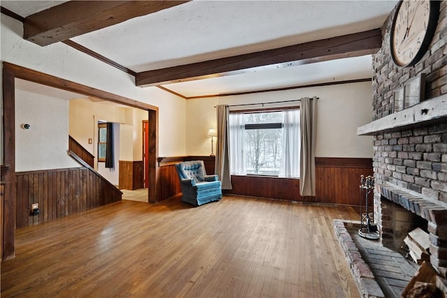 unfurnished living room with wooden walls, a wainscoted wall, light wood-style flooring, beamed ceiling, and a fireplace