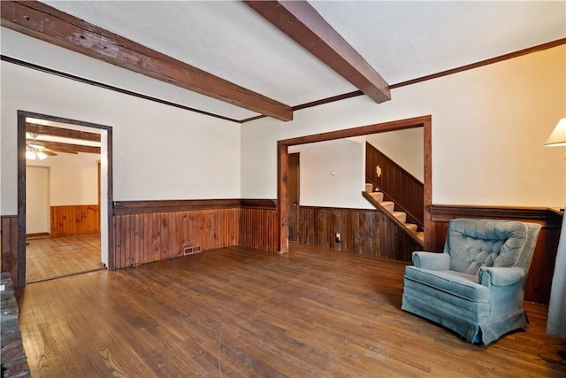 unfurnished room featuring wainscoting, wood walls, wood finished floors, beamed ceiling, and stairs