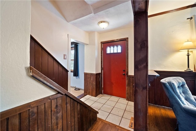 foyer featuring light tile patterned flooring, wainscoting, wooden walls, a textured ceiling, and stairs