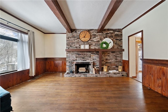 unfurnished living room featuring a wainscoted wall, a brick fireplace, light wood finished floors, and beamed ceiling