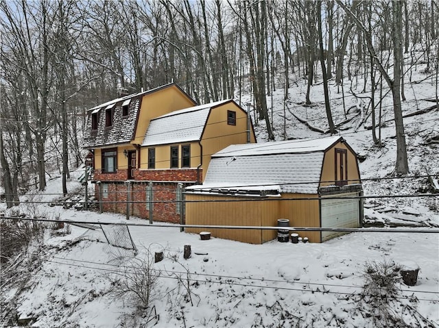 snow covered back of property featuring a detached garage, a gambrel roof, and fence