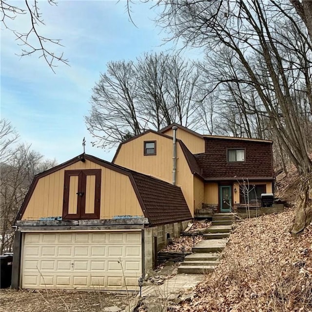 view of front of house featuring a garage, central air condition unit, a shingled roof, and a gambrel roof