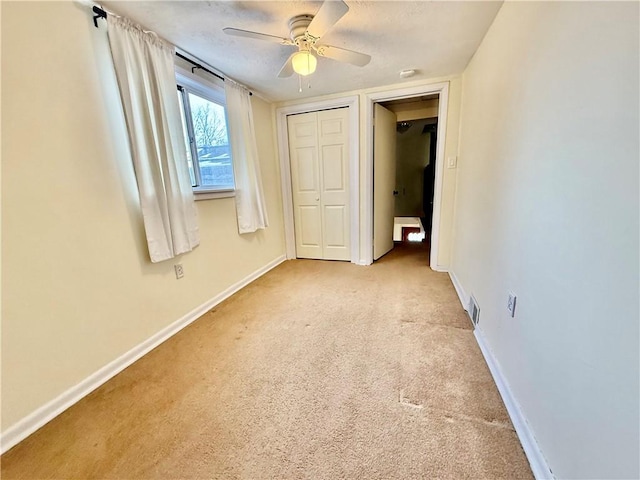 unfurnished bedroom featuring baseboards, ceiling fan, a closet, and light colored carpet