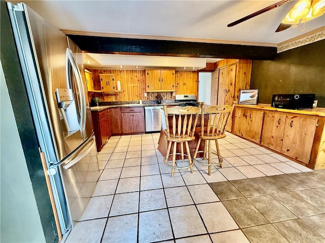 kitchen with ceiling fan, a breakfast bar area, light tile patterned flooring, appliances with stainless steel finishes, and brown cabinetry