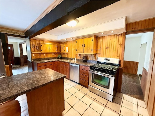 kitchen with dark countertops, appliances with stainless steel finishes, light tile patterned flooring, a sink, and wood walls