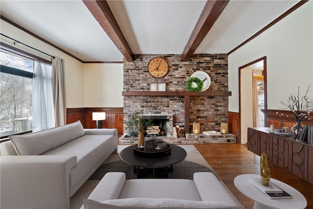 living area featuring wooden walls, wood finished floors, wainscoting, a brick fireplace, and beamed ceiling