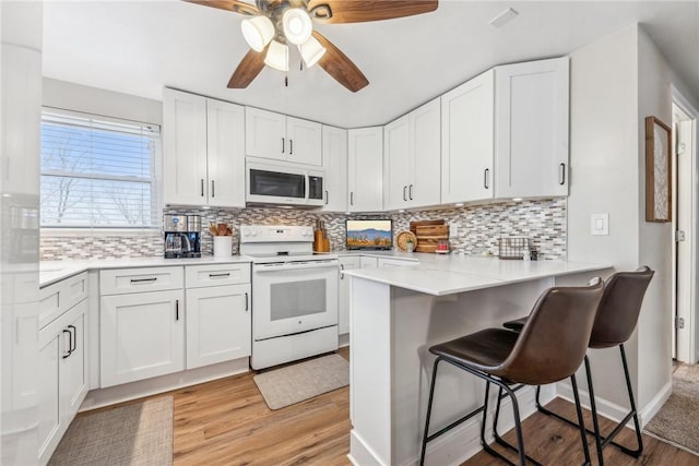 kitchen with a breakfast bar, white appliances, white cabinets, and kitchen peninsula