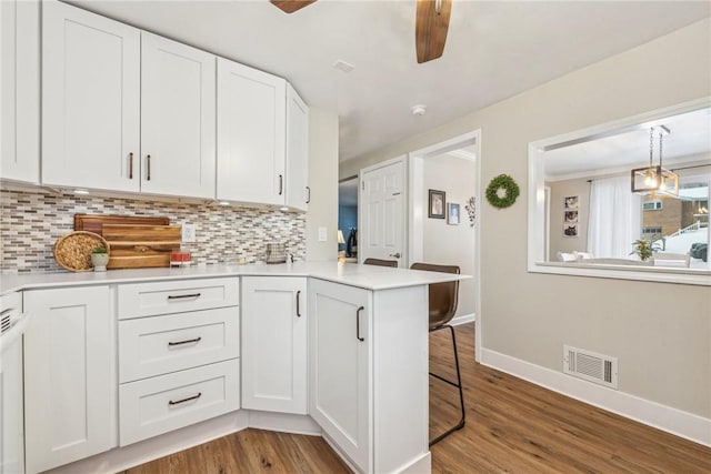 kitchen with light wood-type flooring, kitchen peninsula, decorative backsplash, and white cabinets