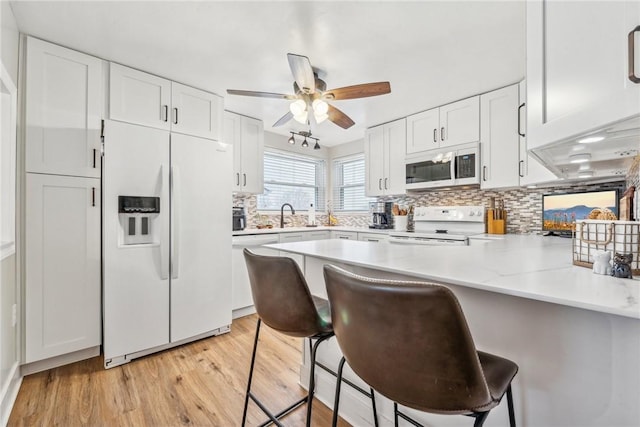 kitchen with tasteful backsplash, a breakfast bar, kitchen peninsula, white appliances, and white cabinetry