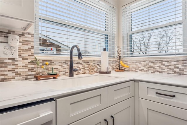 kitchen with light stone countertops, white cabinetry, backsplash, and sink