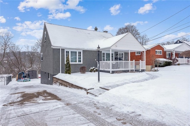 snow covered rear of property featuring covered porch and a storage unit