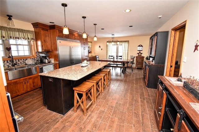 kitchen featuring a center island, sink, hanging light fixtures, stainless steel built in refrigerator, and a breakfast bar area