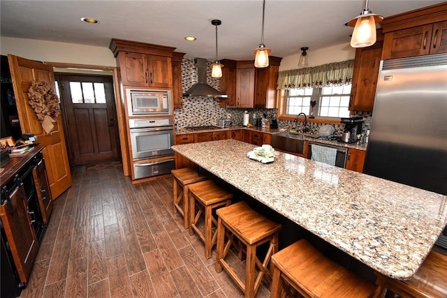 kitchen with decorative light fixtures, appliances with stainless steel finishes, a center island, and wall chimney exhaust hood