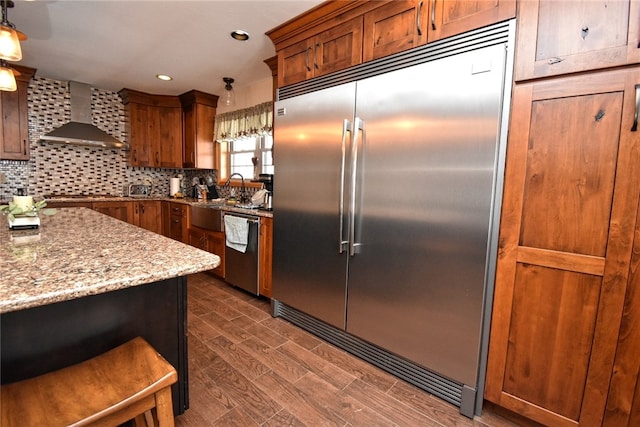 kitchen with decorative light fixtures, backsplash, wall chimney range hood, sink, and appliances with stainless steel finishes