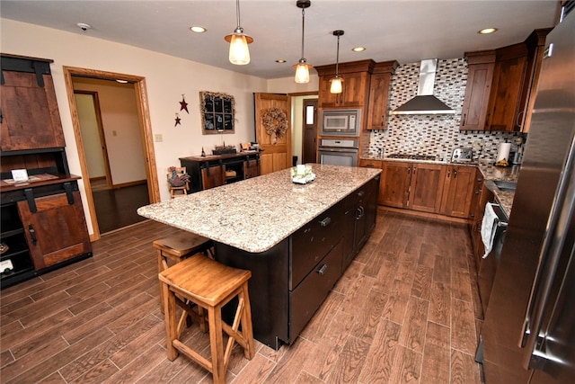 kitchen featuring stainless steel appliances, backsplash, hanging light fixtures, wall chimney range hood, and a center island