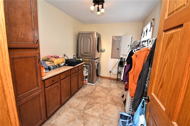 clothes washing area with stacked washer / drying machine, electric panel, and cabinets