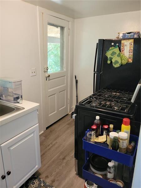 kitchen with light hardwood / wood-style flooring, white cabinets, black fridge, and gas range oven