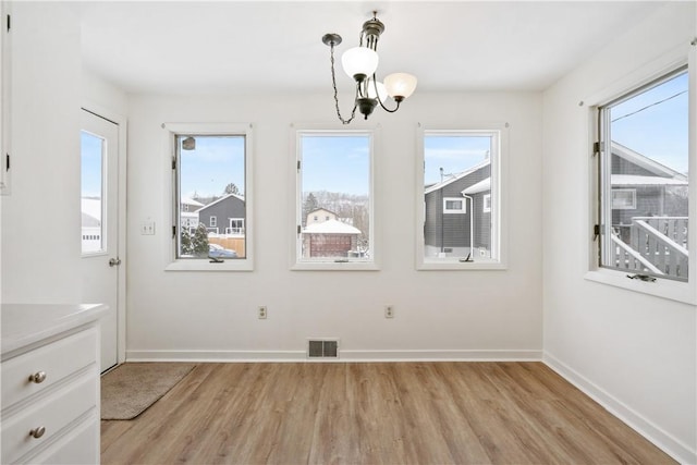 unfurnished dining area with light wood-type flooring, a wealth of natural light, and a chandelier