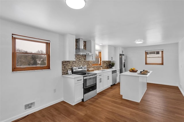 kitchen with white cabinetry, stainless steel appliances, tasteful backsplash, wall chimney exhaust hood, and a center island