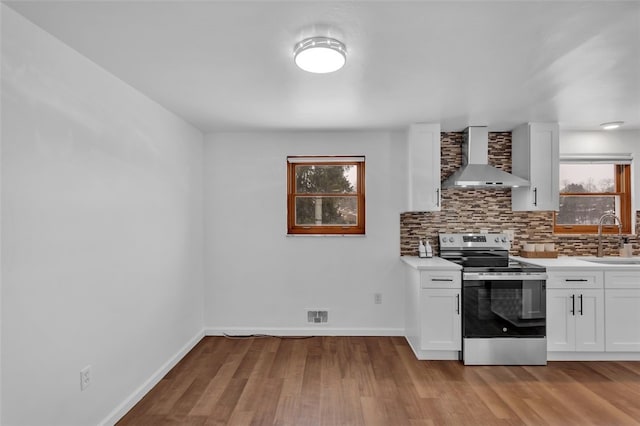 kitchen featuring backsplash, wall chimney range hood, white cabinets, and stainless steel electric range oven