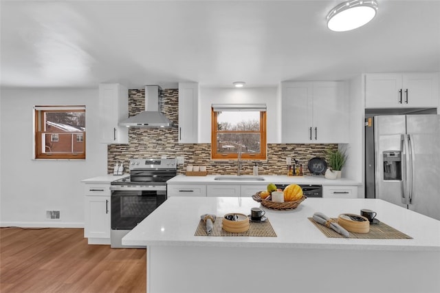 kitchen with appliances with stainless steel finishes, wall chimney exhaust hood, white cabinets, and sink