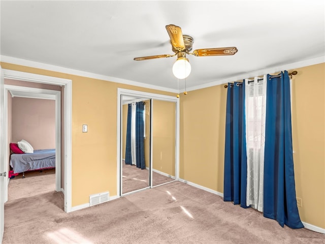 unfurnished bedroom with ceiling fan, a closet, ornamental molding, and carpet flooring