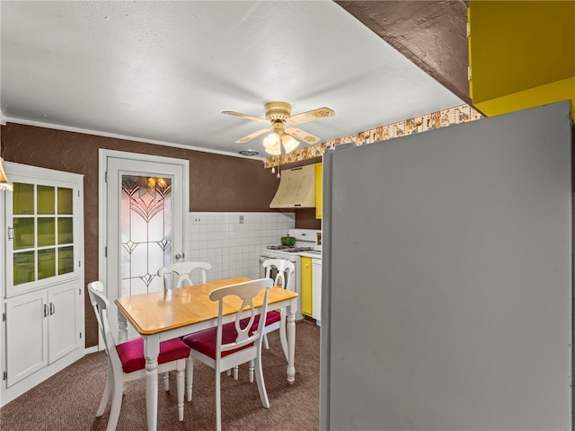 carpeted dining room featuring ceiling fan, tile walls, and ornamental molding